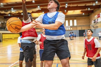 Two basketball players jumping for a rebound during a fast paced indoor court game, showcasing
