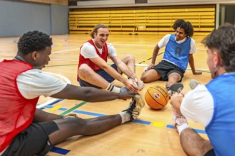 Four happy basketball players stretching their legs on the court before a game, showing teamwork