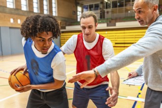 Basketball coach explaining game strategy using clipboard to two players wearing training bibs