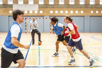 Group of young basketball players running on the court during practice, with their coach watching