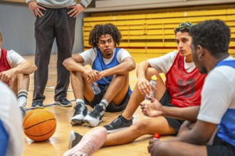 Basketball team resting and drinking water while listening to coach during time out in high school