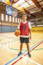 Young basketball player standing confidently on the court, holding a basketball, ready for the game