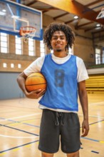 Smiling basketball player holding a ball while standing confidently on the court of an indoor
