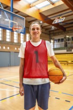 Smiling basketball player holding a ball while standing on an indoor court, exuding energy and