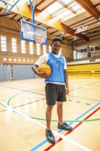 Young male basketball player holding a ball while standing confidently on an indoor court,