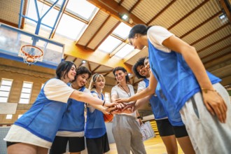 Female basketball players and their coach stacking hands, demonstrating teamwork and unity before a