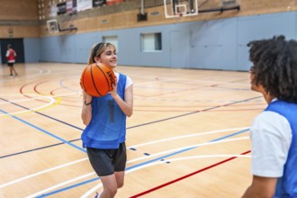 Two basketball players training on the court, with a young woman skillfully passing the ball to her