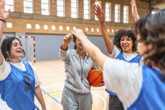 Happy basketball players and their coach celebrating a victory, giving high fives in the court