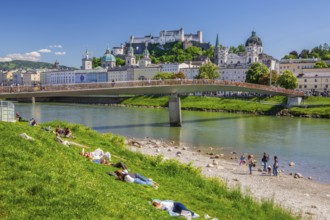 Sunbathers on the banks of the Salzach river next to Hohensalzburg Fortress, Salzburg, Salzach
