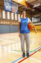 Young woman basketball player standing on the court holding a ball under her arm, ready for the