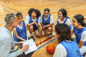 Female basketball team listening to their coach explaining game strategy on a clipboard during a
