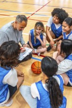 High angle view of a basketball coach drawing a play on a clipboard while sitting on the court with