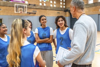 High school girls basketball team listening to their coach explain game strategy on a clipboard in