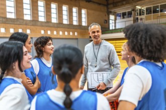 Basketball coach holding clipboard and explaining game strategy to a group of female athletes in a
