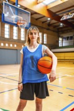 Young female basketball player standing on the court, holding a basketball, ready for the game,
