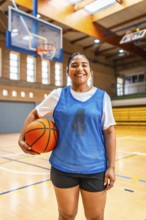 Young female athlete wearing blue jersey and black shorts, holding basketball and smiling in an