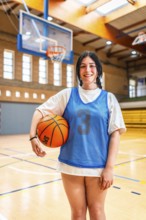 Female athlete smiling and holding basketball in a gymnasium, ready for training or competition