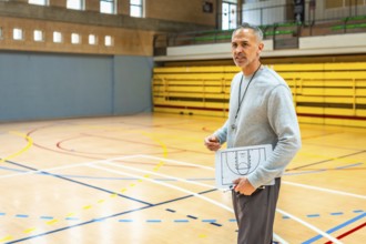 Mature basketball coach holding clipboard with game strategy explaining tactics to team players in