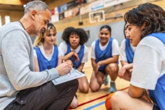 Basketball coach drawing a play on a clipboard and explaining game strategy to his female team