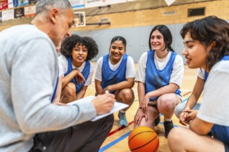 Basketball coach briefing his female team during a time out, taking notes and discussing game