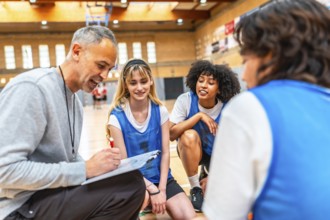 Basketball coach drawing a play on clipboard and explaining game strategy to his multi ethnic