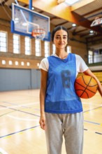 Young woman basketball player standing confidently on the court, holding a ball and embodying