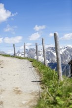 Narrow path with wooden posts at the edge, leads through an alpine landscape with snow-covered