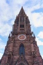 Freiburg Minster, Gothic church tower made of red stone with clock in front of a blue sky, Freiburg