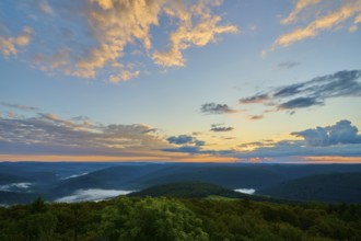 Sunrise with dramatic clouds behind wooded hills, golden light in the sky, Katzenbuckel, Waldbrunn,