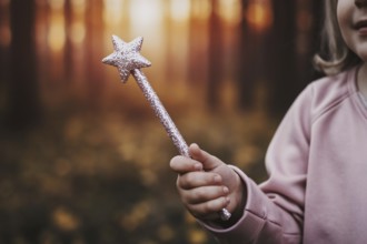 Close-up of pink glittering fairy wand with star tip held by young girl's hand, magical children's