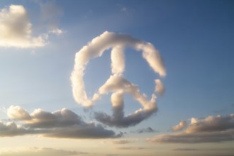 A naturally formed peace sign made of white clouds floats in a clear blue sky, symbolizing harmony