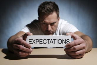 Man holding block labeled expectations, symbolizing social pressure and masculine burden.