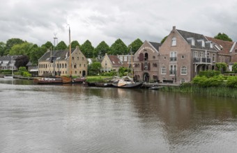 Tranquil river landscape with boats and brick buildings under a cloudy sky, Dokkum, Friesland,