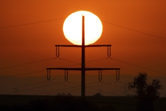 The sun rises behind an electricity pylon near Frankfurt am Main, Frankfurt am Main, Hesse, Germany