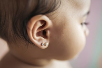 Two delicate diamond stud earrings in baby's ears bathed in warm golden light. Tender moment with