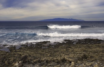 Coast with turbulent waves in front of a distant island (La Gomera) on the horizon, Tenerife,