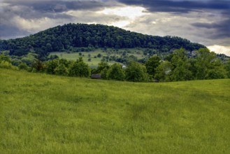 Hilly landscape with wide green meadows and wooded areas under a cloudy sky, Bad Boll,