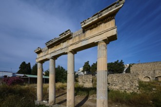 Three ancient columns with a fragment of the entablature, surrounded by ruins and blue sky, Xysto
