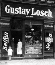Soap shop, 1910, A man, a woman and a child stand in front of an old soap shop with a large sign