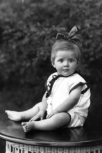 Little girl sitting on a table with a bow in her hair, portrait of a baby with a bow in children's