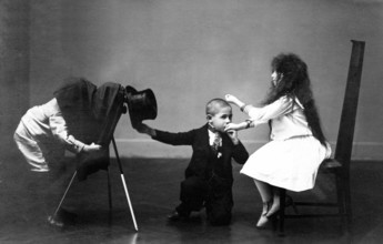 Children photograph hand kiss, 1920, A boy in suit and top hat playing with two other children, one