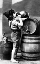Child drinking wine, 1910s, A boy in traditional dress drinks from a large jug next to beer
