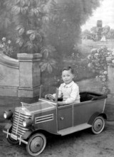 Little boy in car, 1930s, A boy sits in a toy car in front of a picturesque background, Historical
