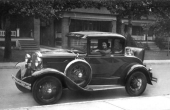 Woman in vintage car children, 1930s, A vintage car with passengers drives along a street with