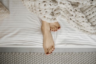 Bare feet with red nail polish rest on crisp white sheets, partially covered by a soft, knitted