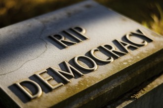 Old tombstone in ground with text RIP Democracy. Visual metaphor for the decline of democratic