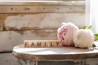 Wooden blocks spelling family beside peony flowers. A warm symbol of love, togetherness, and cozy