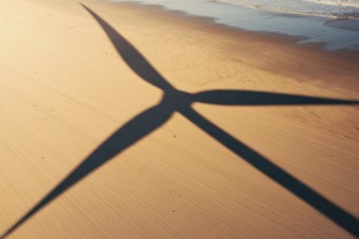 Wind turbine shadow on sunlit beach. A poetic symbol of clean energy blending with nature.