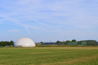 Field with a biogas plant and wind turbines under a blue sky, Germany