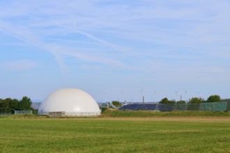 Biogas plant with wind turbines in the background, wide green field, Germany